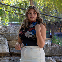 Woman standing outdoors with a stone wall and greenery in the background