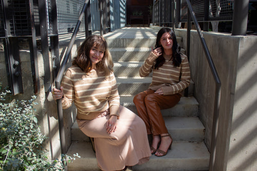 Two women sitting on concrete steps outdoors, wearing matching striped sweaters.
